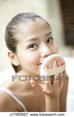 Stock Photo - Front view of a young woman holding powder puff close to face.. Fotosearch