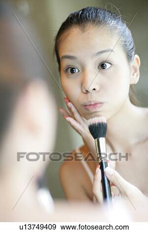 Stock Photo - Mirror image of a young woman applying foundation.. Fotosearch