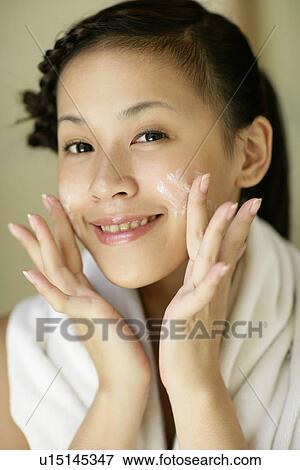 Stock Photo - Portrait of a young woman applying a cream on face.. Fotosearch