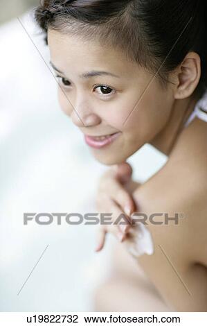 Stock Image - View of a young woman applying a cream on a body.. Fotosearch