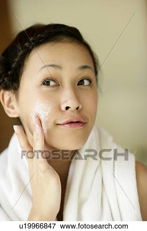 Stock Photo - View of a young woman applying a cream on her face.. Fotosearch