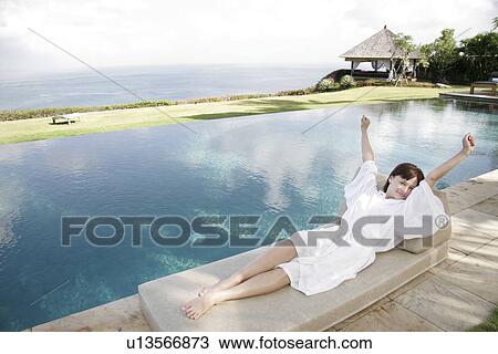 Stock Image - Young woman lying besides a swimming pool.. Fotosearch