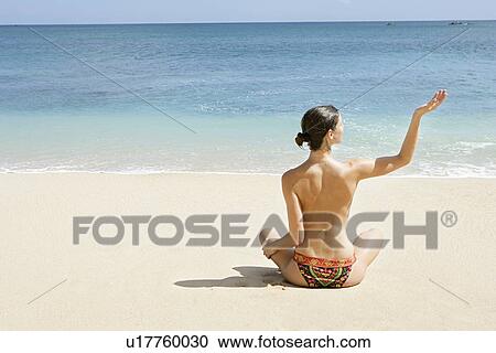 Stock Image - Rear view of a woman exercising on a beach.. Fotosearch