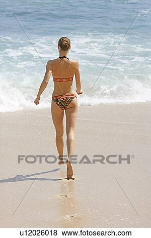 Stock Photo - Rear view of a woman running on a beach.. Fotosearch