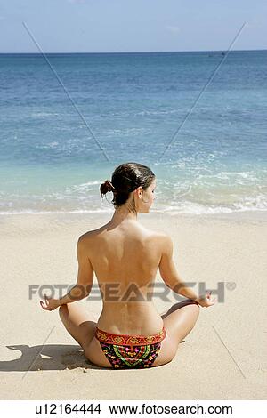 Picture - Rear view of a woman sitting in lotus position on a beach.. Fotosearch