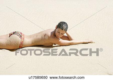 Stock Image - View of a topless woman lying on a beach.. Fotosearch