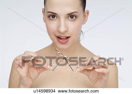 Picture - Close-up of a young woman holding eyelash curler. Fotosearch