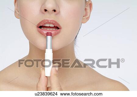 Picture - View of a young woman applying lipstick.. Fotosearch