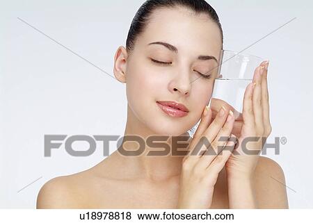 Stock Photo - View of a young woman holding glass of water, eyes closed.. Fotosearch