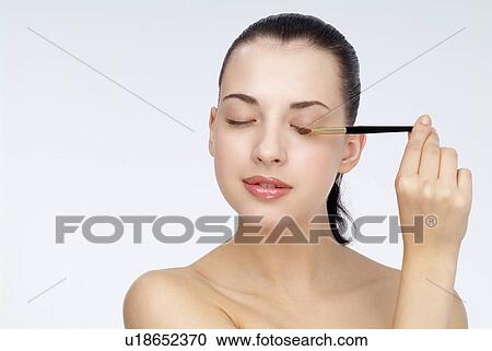Stock Image - View of a young woman using makeup brush.. Fotosearch