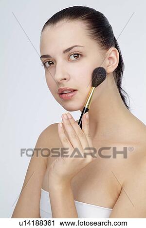 Stock Image - Close-up of a young woman holding makeup brush.. Fotosearch
