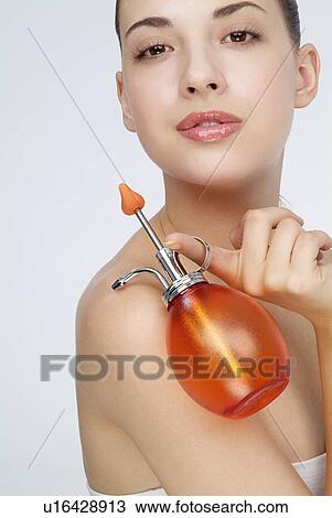 Stock Image - Close-up of a young woman holding perfume bottle.. Fotosearch