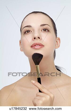 Stock Image - Close-up of a young woman holding makeup brush.. Fotosearch