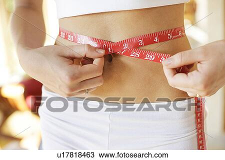 Stock Image - A woman measuring her waist.. Fotosearch