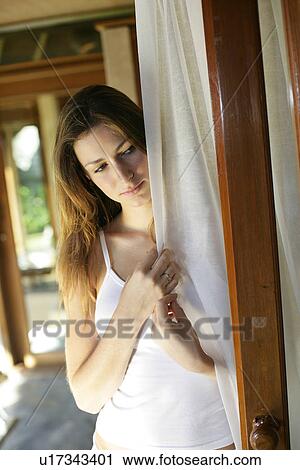 Stock Image - Side view of a woman holding curtain.. Fotosearch