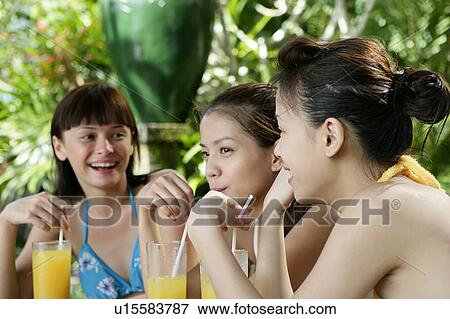 Stock Photo - Three teenage girls with juice glasses, holding straws.. Fotosearch
