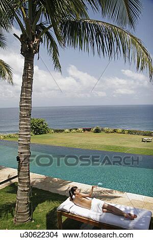 View of a teenage girl sun bathing near a swimming pool. View Large Photo Image Picture - View of a teenage girl sun bathing near a swimming pool.. Fotosearch