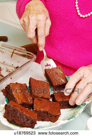 Stock Image - A woman is serving cake bars in a tray.. Fotosearch