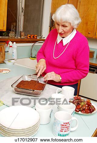 Stock Photo - An elderly woman preparing cake in a kitchen.. Fotosearch