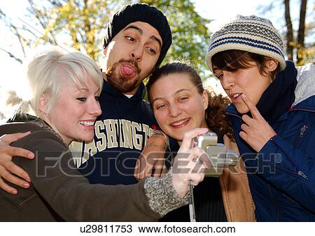Stock Image - Portrait of four people recording themselves on a camcorder.. Fotosearch