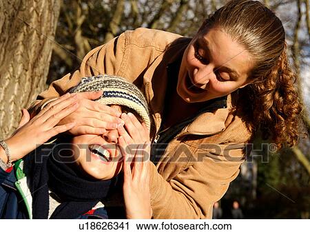 Stock Image - View of a young woman shutting her friends eyes.. Fotosearch