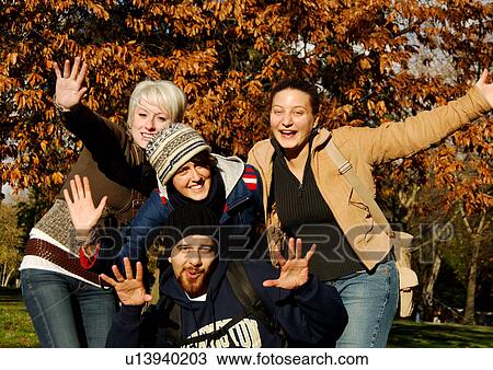 Stock Image - View of four ecstatic friends posing against the camera.. Fotosearch