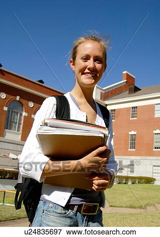 Stock Photo - Portrait of a cheerful young woman holding her books.. Fotosearch