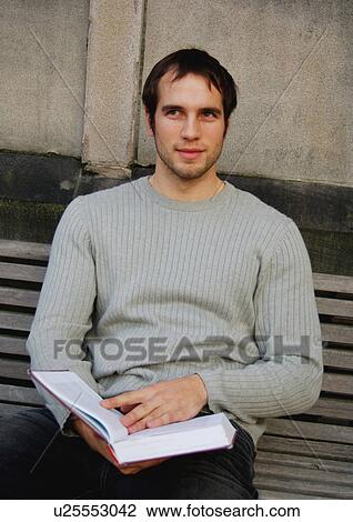 Stock Image - Portrait of a young man reading a book.. Fotosearch