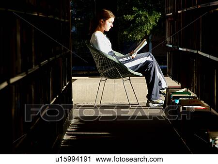 Stock Image - Profile of a young woman reading a book in a library.. Fotosearch
