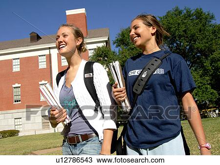 Side view of two young women walking together, holding their books. View Large Photo Image Stock Image - Side view of two young women walking together, holding their books.. Fotosearch