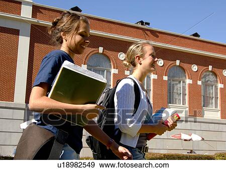 Stock Photo - Side view of two young women walking together, holding their books.. Fotosearch