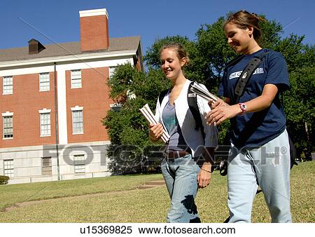 Stock Photography - Side view of two young women walking together, holding their books.. Fotosearch