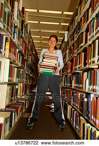View of a woman holding a stack of books in a library. View Large Photo Image Stock Image - View of a woman holding a stack of books in a library.. Fotosearch
