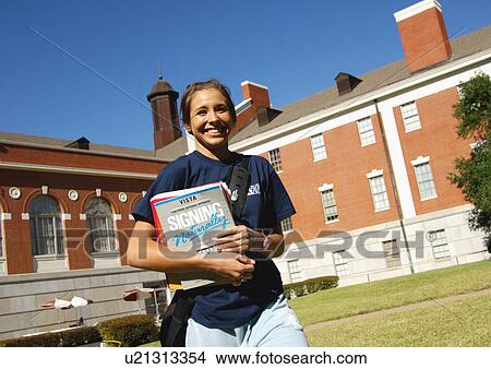 Picture - View of a young woman holding her books, and smiling at the camera.. Fotosearch