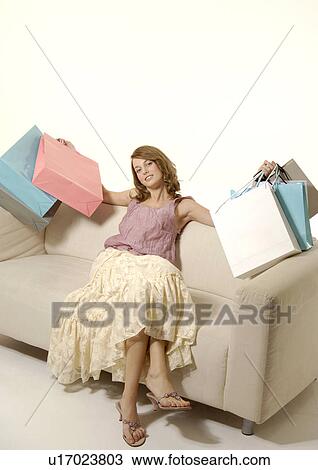Stock Image - Portrait of a woman on a couch with her shopping bags.. Fotosearch