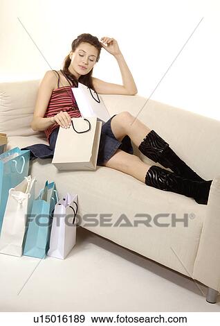 Stock Photo - Portrait of a woman sitting on a couch and looking into her shopping bag.. Fotosearch
