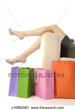 Stock Image - View of a woman lying on a couch with shopping bags placed beside it.. Fotosearch
