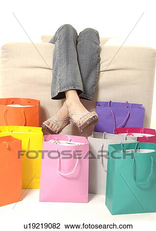 View of a woman lying on a couch with shopping bags placed beside it. View Large Photo Image Stock Image - View of a woman lying on a couch with shopping bags placed beside it.. Fotosearch