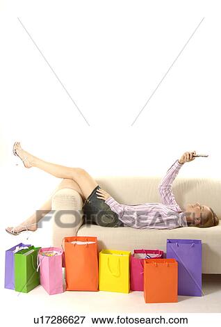 View of a woman lying on a couch with colorful shopping bags placed beside her. View Large Photo Image Stock Photo - View of a woman lying on a couch with colorful shopping bags placed beside her.. Fotosearch