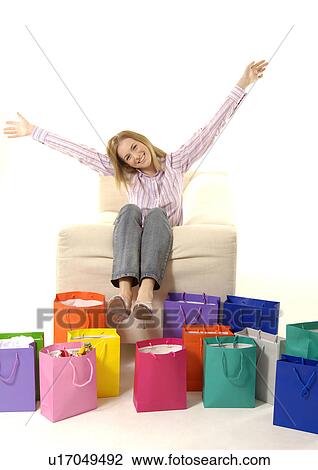 Stock Image - View of a young woman with colorful shopping bags placed in front of her.. Fotosearch