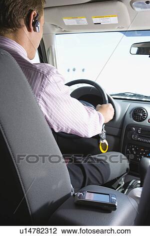 Stock Image - A Businessman Wearing Headset and Driving a Car, Rear View, Three Quarter Length. Fotosearch