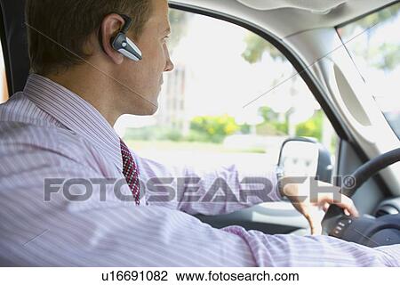 Stock Image - A Businessman Wearing Headset and Driving a Car, Head and Shoulders, Side View. Fotosearch