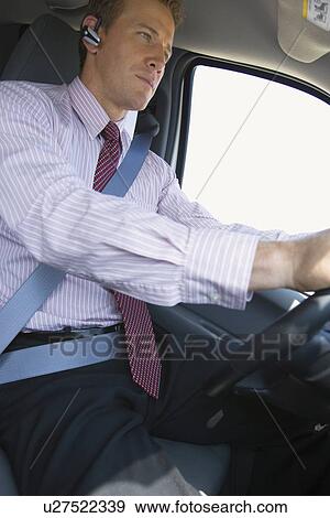 Stock Photo - A Businessman Wearing Headset and Driving a Car, Three Quarter Length. Fotosearch