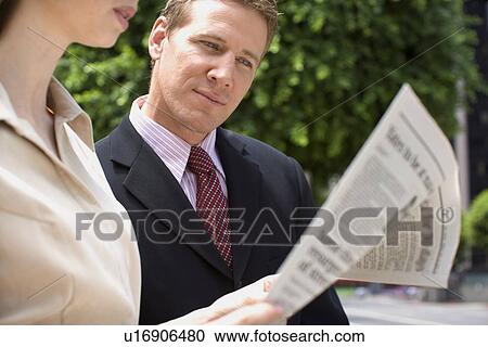 Stock Image - A Mid Adult Businessman Looking into a Newspaper, Waist Up, Differential Focus. Fotosearch