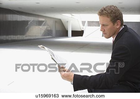 Stock Image - A Mid Adult Businessman Reading a Newspaper, Side View, Three Quarter Length. Fotosearch