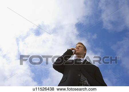 A Mid Adult Businessman Talking on a Cellular Phone, Low Angle View, Waist Up View Large Photo Image Stock Photo - A Mid Adult Businessman Talking on a Cellular Phone, Low Angle View, Waist Up. Fotosearch
