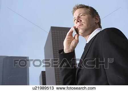 Stock Image - A Mid Adult Businessman Talking on the Cellular Phone, Low Angle View, Waist Up. Fotosearch