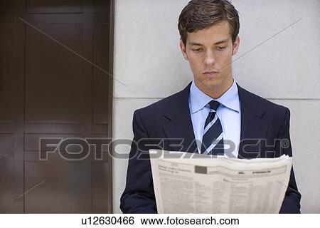 Stock Photograph - A Young Adult Businessman Reading a Newspaper, Front View, Waist Up. Fotosearch