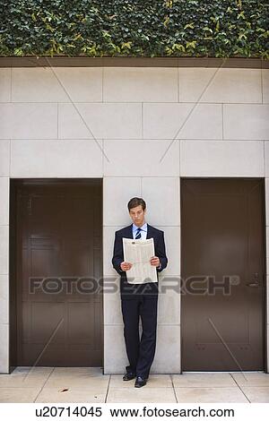 Stock Photography - A Young Adult Businessman Reading a Newspaper, Front View, Full Length. Fotosearch