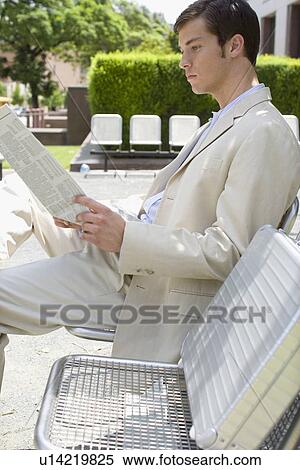 A Young Adult Businessman Sitting on a Chair and Reading a Newspaper, Side View, Three Quarter Length View Large Photo Image Stock Photography - A Young Adult Businessman Sitting on a Chair and Reading a Newspaper, Side View, Three Quarter Length. Fotosearch